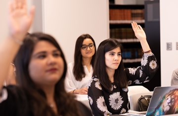 Three students sitting in a class, two raising hands while one smiling and listening to the talk