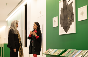 Professor Zayn Kassam listening to a lady explaining the image from the climate change exhibition in AKC gallery